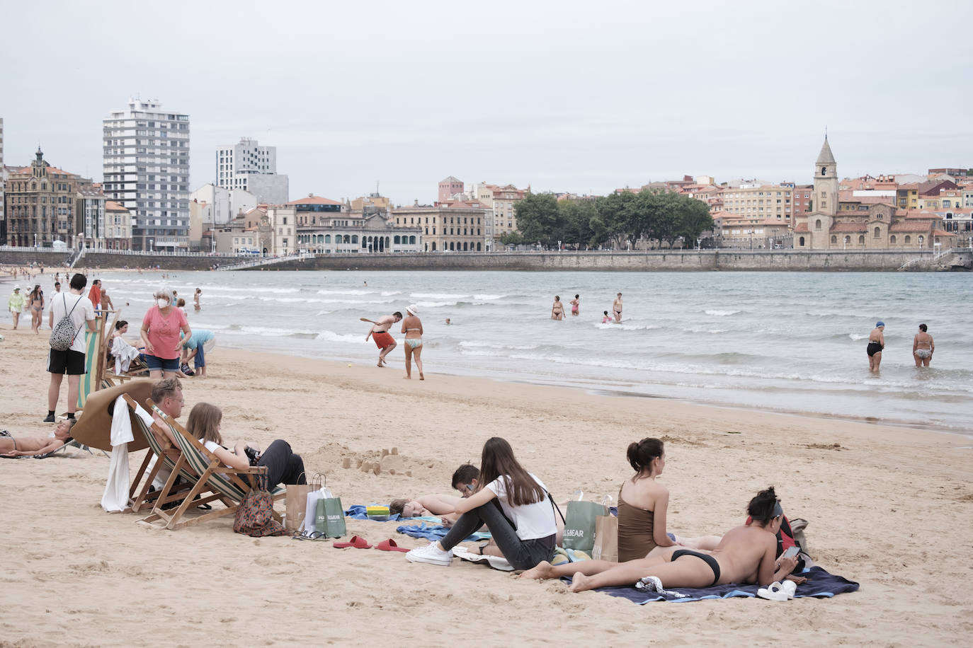 Está siendo un verano atípico en la costa asturiana, pero el mal tiempo no ha impedido que los bañistas se lancen a la playa de San Lorenzo con ganas de disfrutar del día. Algunos pasean, otros leen con la ropa puesta y los más valientes se atreven a darse un chapuzón. Cualquier plan es preferible a quedarse en casa.