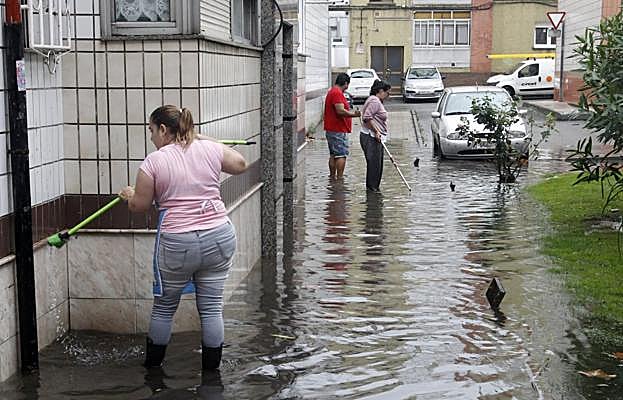 Tres vecinos de la calle Brasil se esfuerzan por aliviar el agua embalsada con unas escobas. 