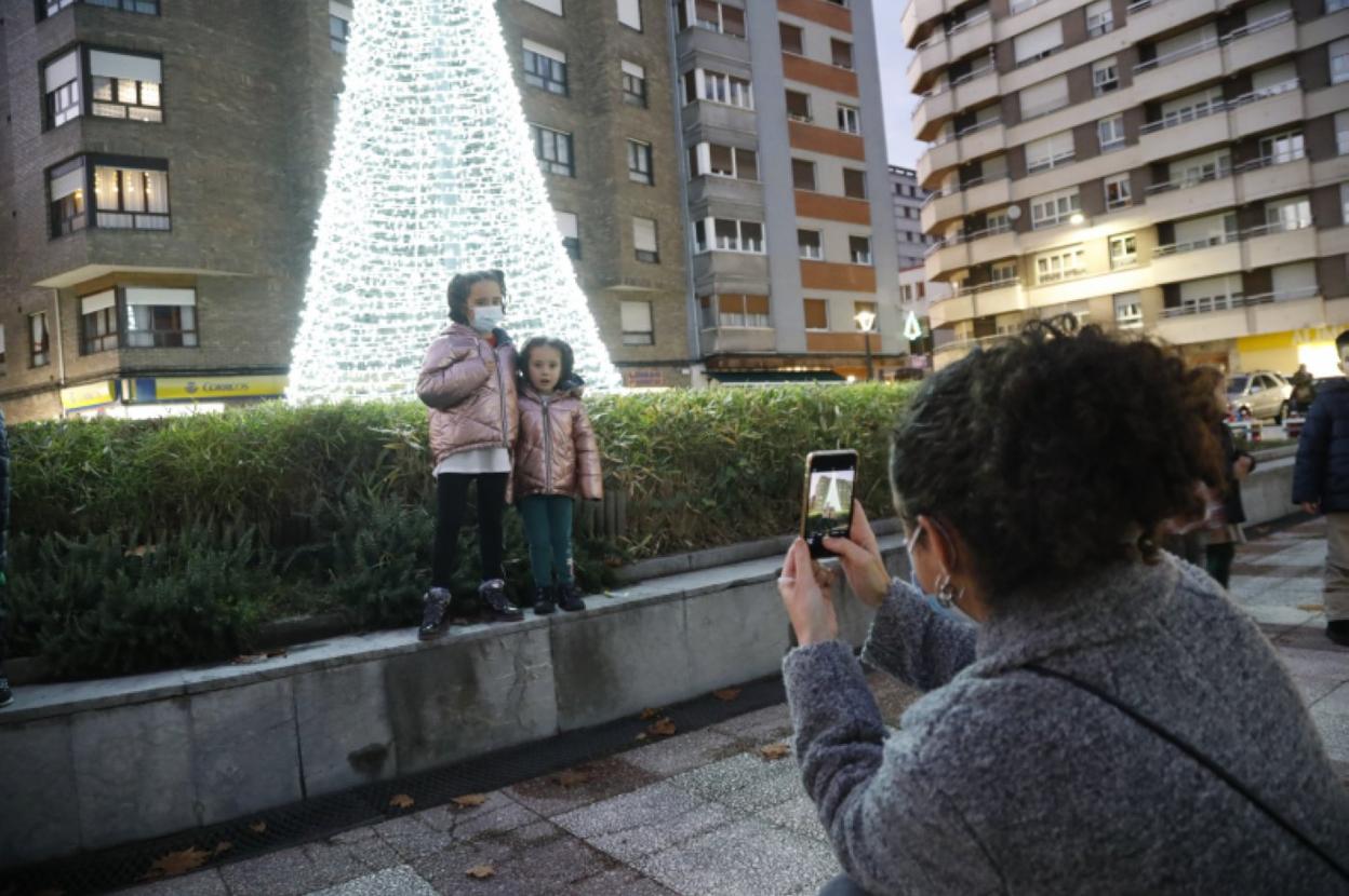 Una mujer fotografía a dos niñas junto al árbol, ya encendido. 