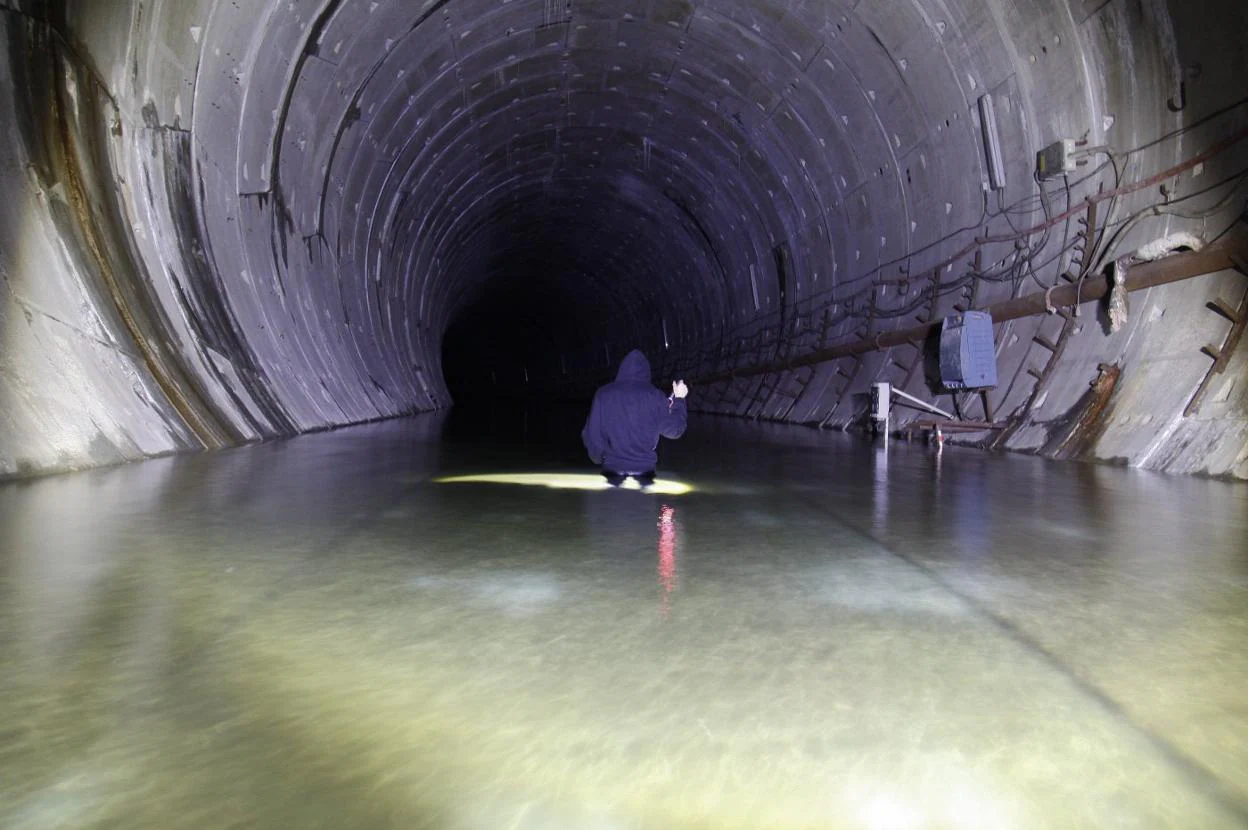 El interior. Un miembro de Podemos, metido en el agua en el interior del túnel del metrotrén, en diciembre de 2016. Las entradas. A la izquierda, acceso al metrotrén junto al Museo del Ferrocarril. A la derecha, entrada al túnel en Justo del Castillo. 