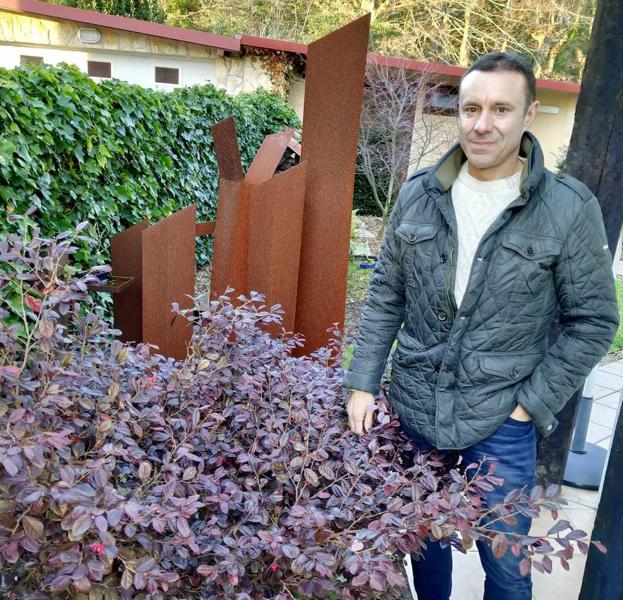 Mario Argüelles, ante un purpúreo loropetalum chino, muestra su escultura Umbral Botánico en la transición al jardín japonés.