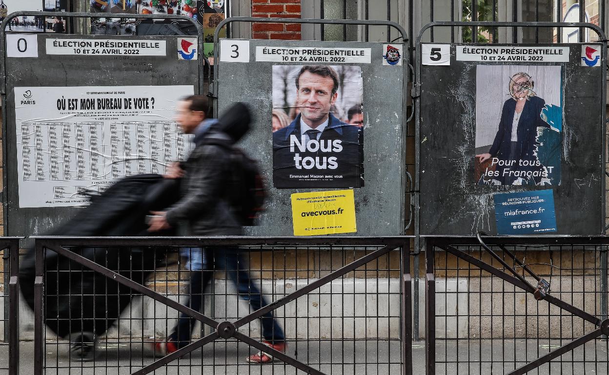 Un hombre transita con un violonchelo junto a carteles electorales de Macron y Le Pen colocados en una calle de París.. 