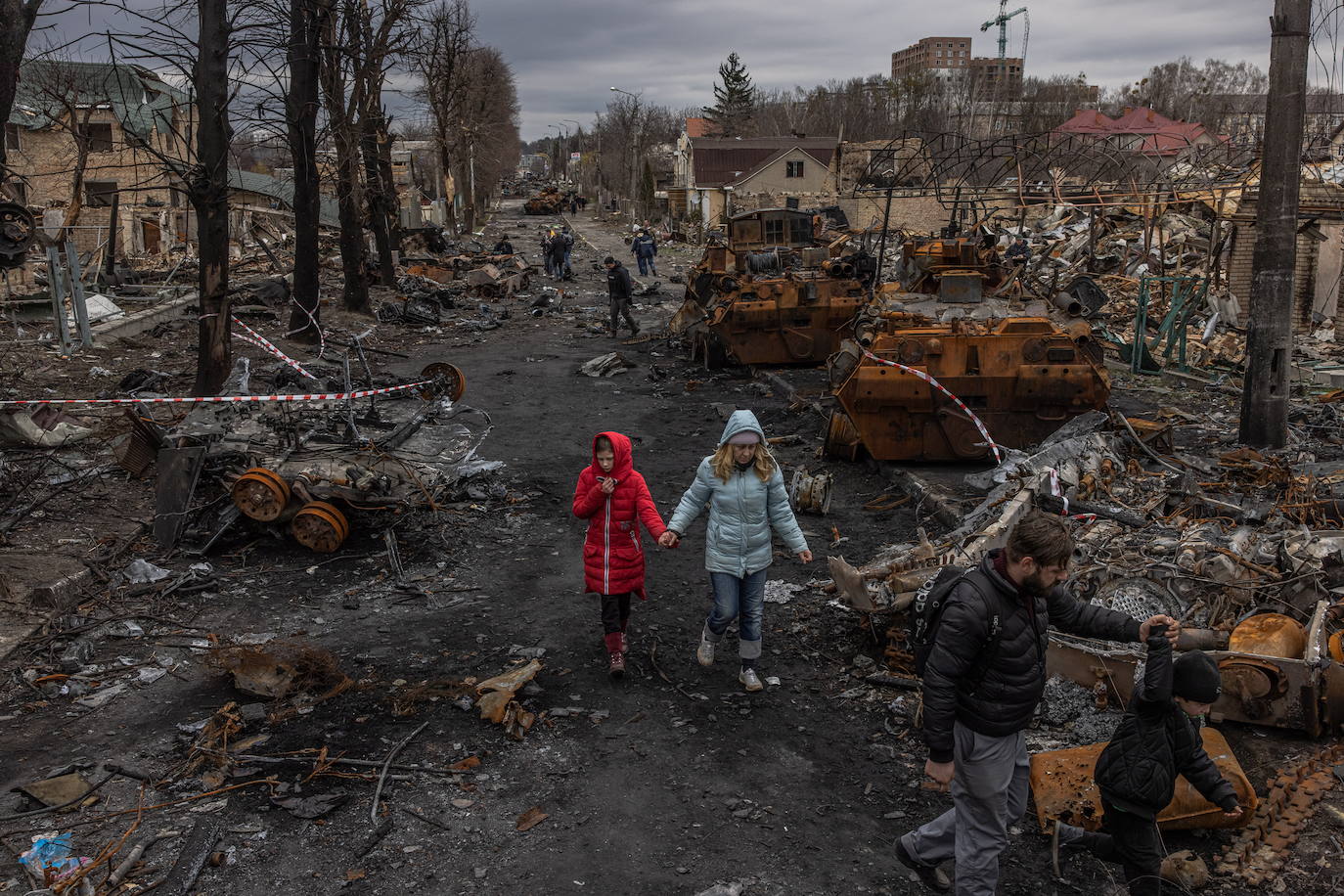 En la imagen, una familia camina por las calles destrozadas de Bucha. En el vídeo, los habitantes de la ciudad ucraniana lloran a sus muertos 