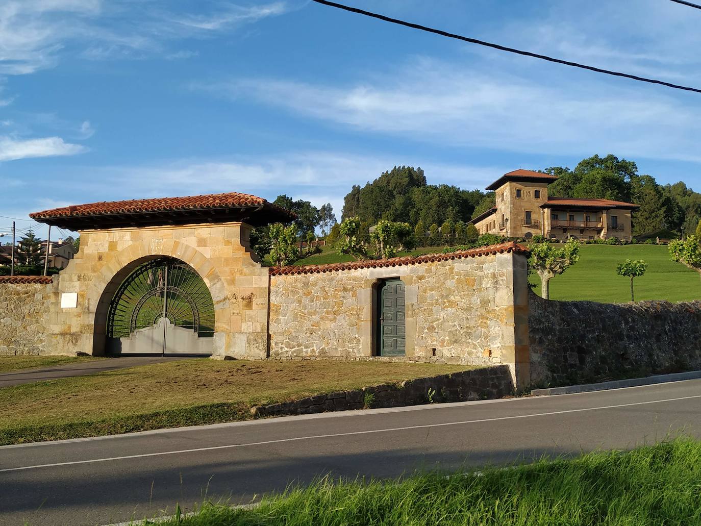 Nuevo acceso principal a La Riega con los tilos sobresaliendo, la extensa pradera y la casa señorial al fondo.