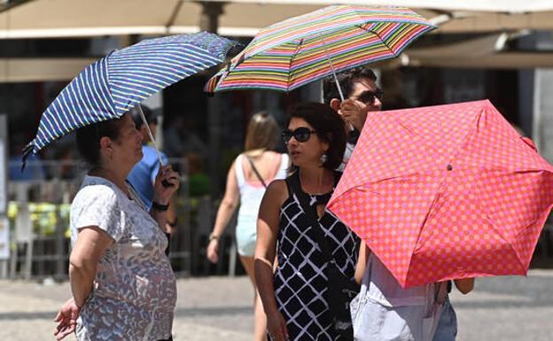 Varias personas pasean con una sombrilla por el centro de Madrid.