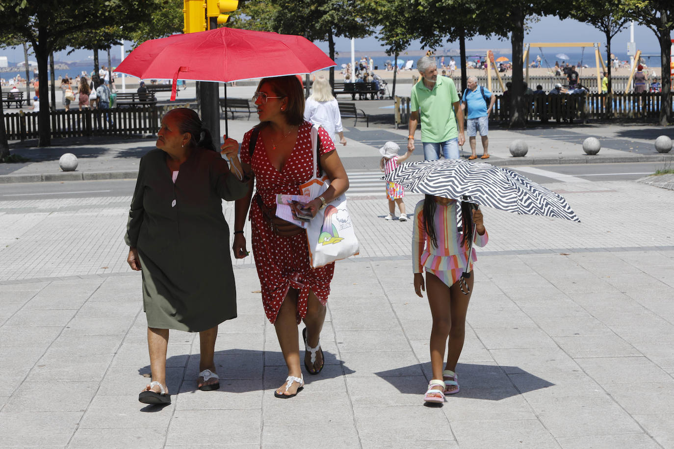  Dos mujeres y una niña pasean por Gijón protegidas del sol con un paraguas. 