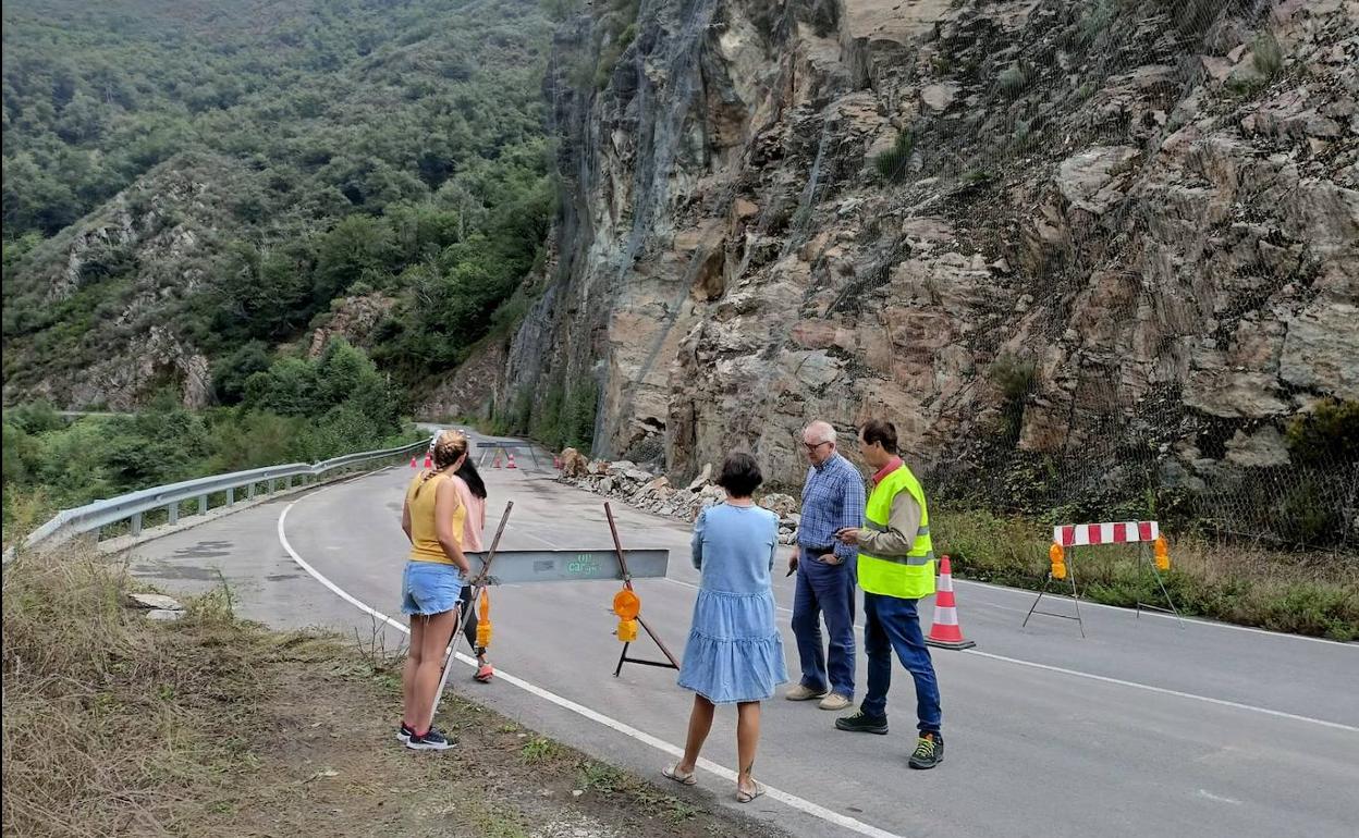 Varias personas observan las rocas retiradas a un lado de la carretera. 