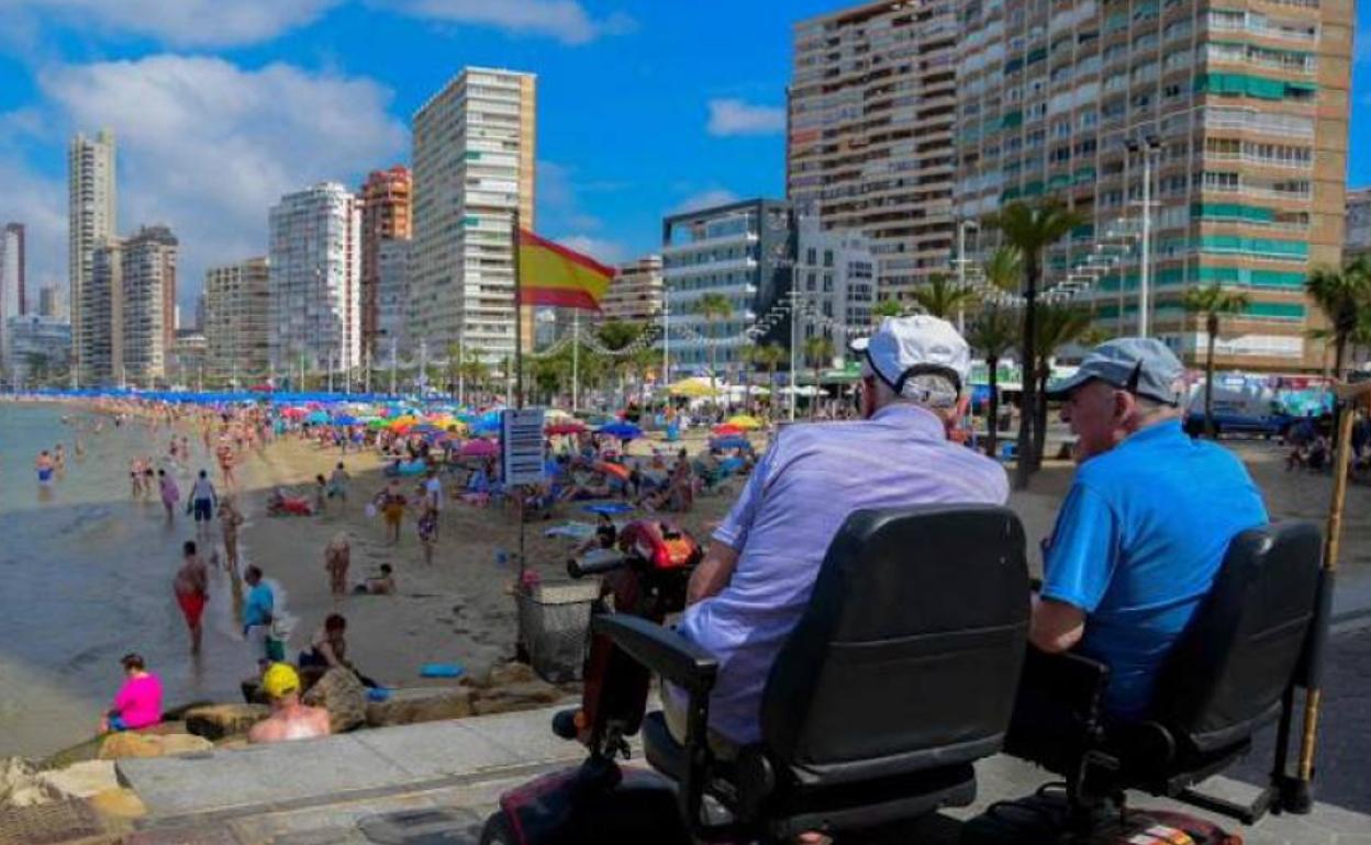 Dos mayores disfrutan del sol ante la playa. 