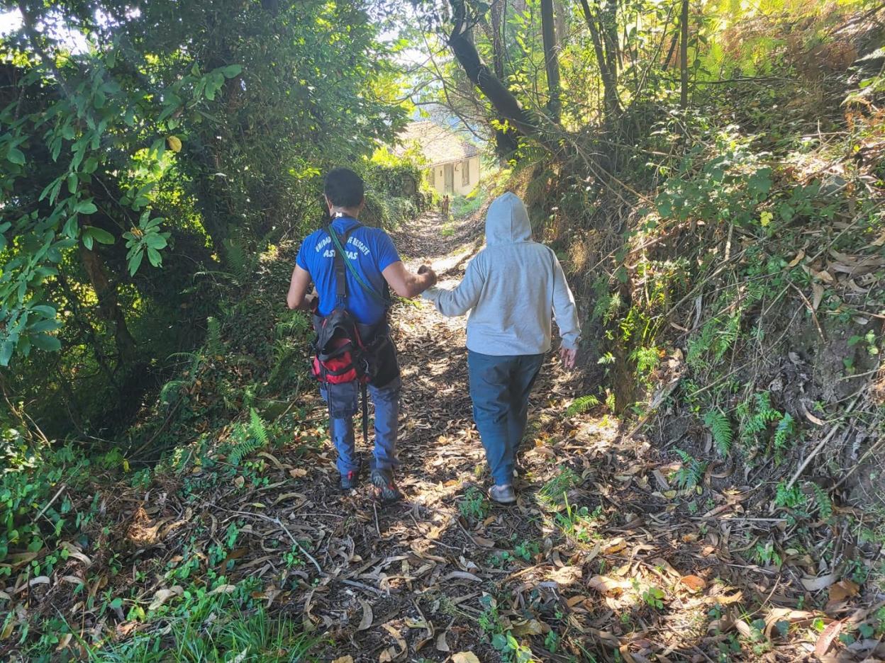 Un voluntario de la Unidad Canina ayuda a caminar a la mujer de vuelta a casa, precedidos ambos del perro que la localizó, 'Chuli'. 