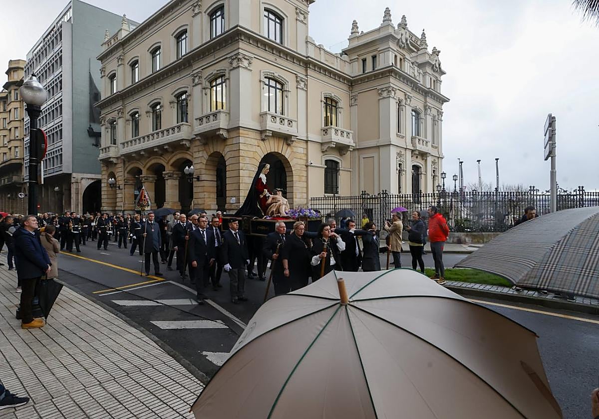 Momento en que el traslado público de la imagen de La Piedad al pie de la Cruz enfila los Jardines de la Reina con espectadores protegiéndose de la lluvia con paraguas.
