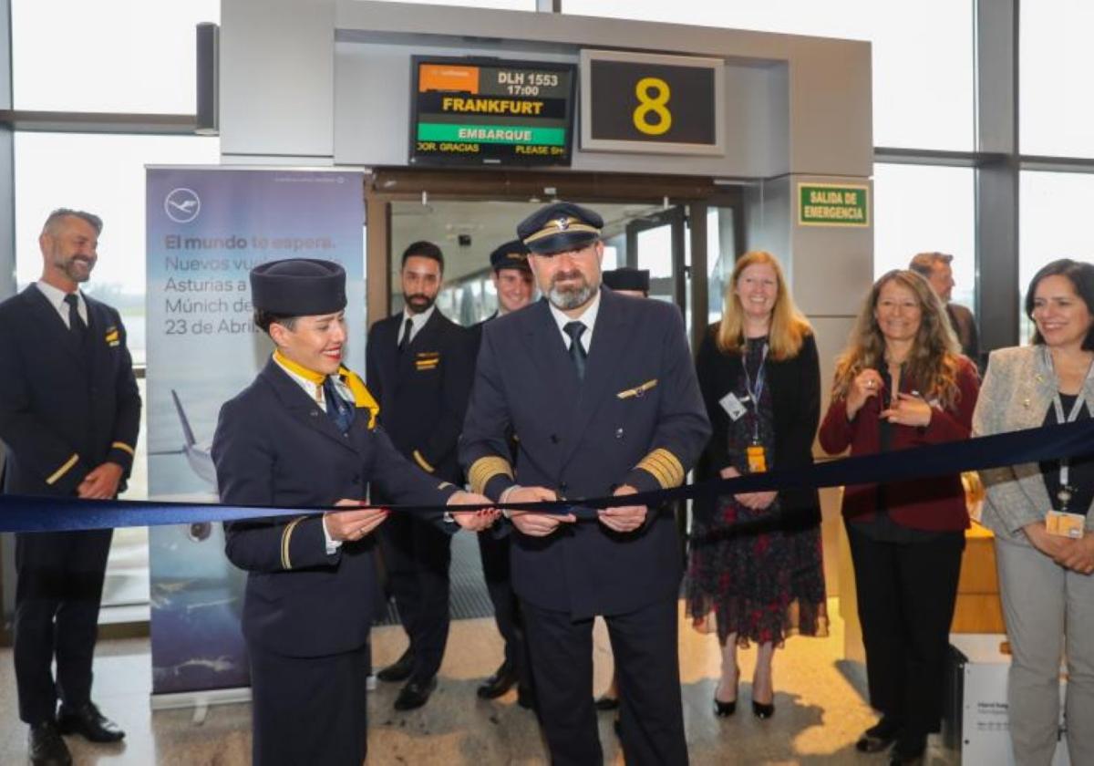 El comandante Miguel Martín-Veysada y la jefa de cabina, Claudia Kübler, cortan la cinta inaugural del primer vuelo de Lufthansa a Asturias, en la zona de embarque del aeropuerto, ante representantes de la compañía y el resto de la tripulación.