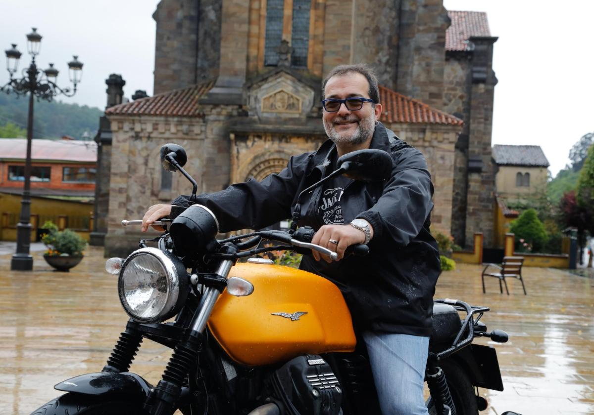 Roberto García, sobre una moto prestada, ante la iglesia de Ciaño, de la que fue párroco.