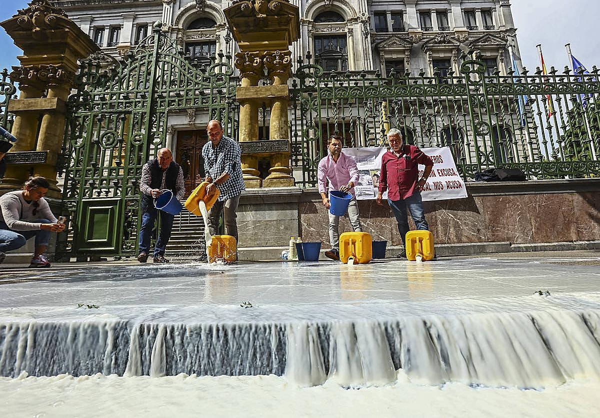 Representantes del sector ganadero derraman leche a la entrada de la Junta General del Principado, como protesta por la propuesta de bajada del precio por litro producido.