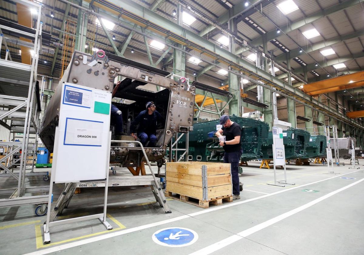 Dos operarios de la fábrica de armas de Trubia trabajan en la línea de pintura de los blindados, en concreto con una barcaza del VCR 8x8 Dragón, junto a varias unidades del Castor.