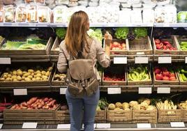 Una mujer frente a un estante de verduras y hortalizas.