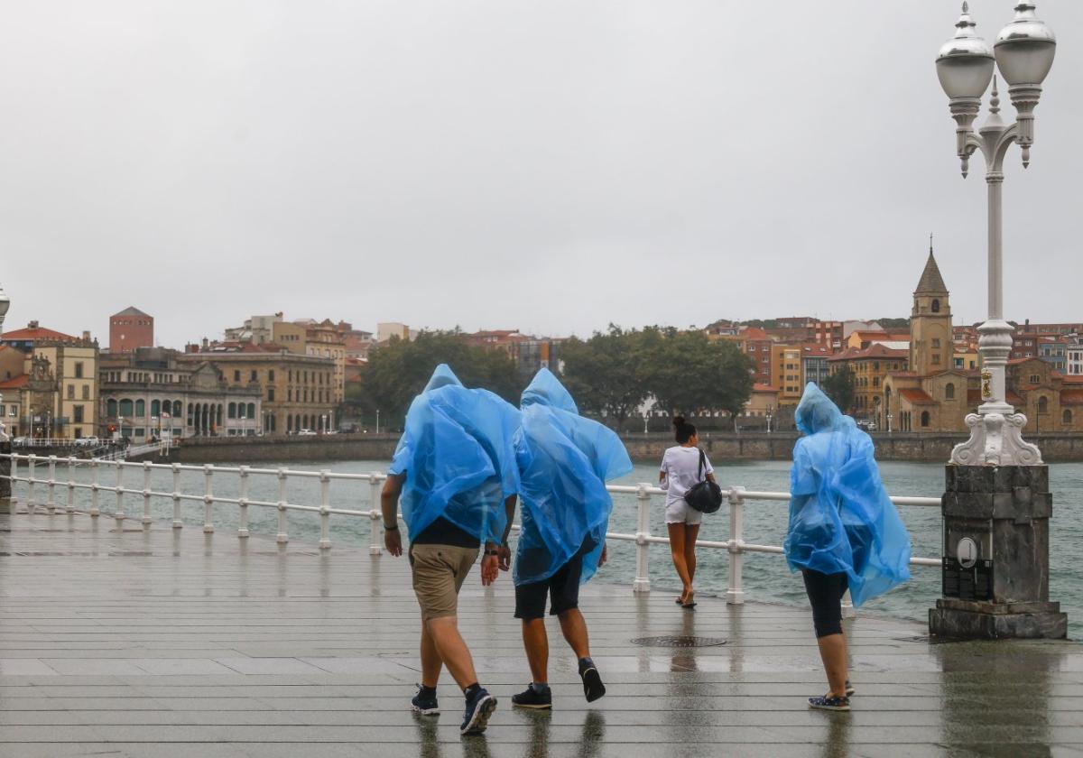 Unos turistas de paseo por el Muro se resguardan bajo unos chubasqueros de la lluvia del pasado viernes.