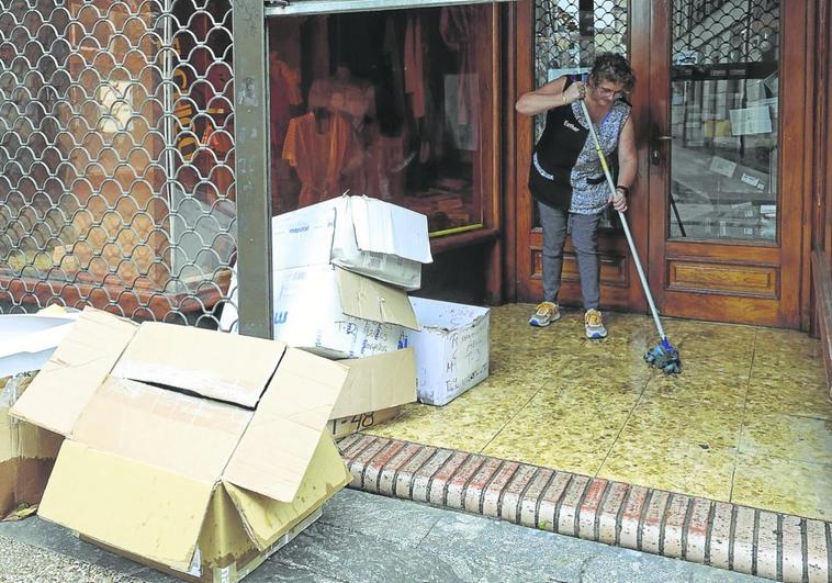 Tienda El Chico. Esther López friega la entrada de su negocio inundado por la lluvia que cayó con intensidad durante la noche, y saca las cajas mojadas.