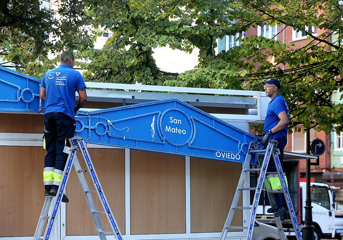 Dos operarios desinstalan uno de los letreros de las casetas hosteleleras de San Mateo.