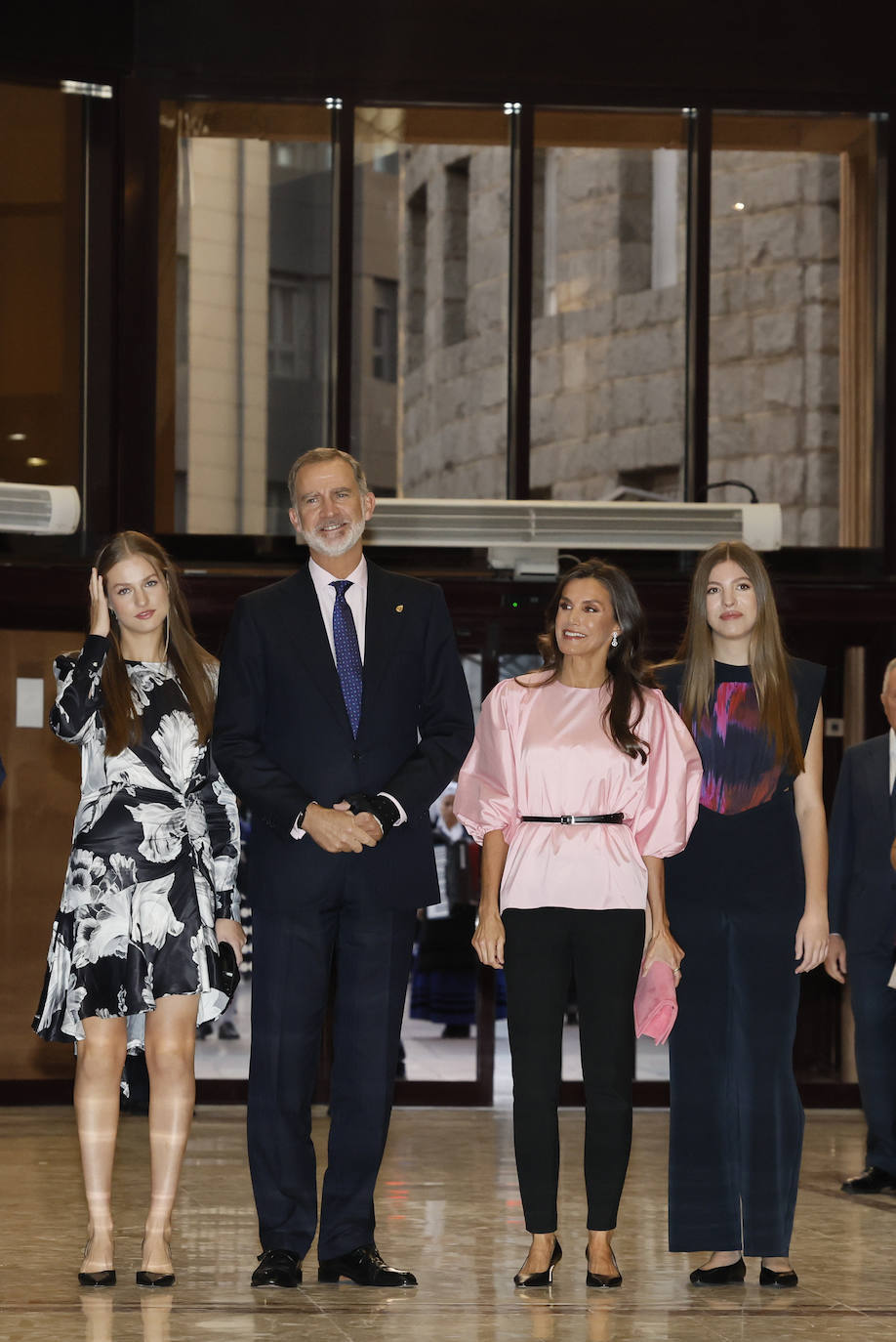 la Reina Letizia apostó por un pantalón negro 'slim fit' tobillero, combinado con una blusa satinada de color rosa con mangas abullonadas. Los complementos de doña Letizia fueron unos salones negros con tacón comedido y una cartera de mano de color rosa, un par de tonos más fuertes que la blusa. 