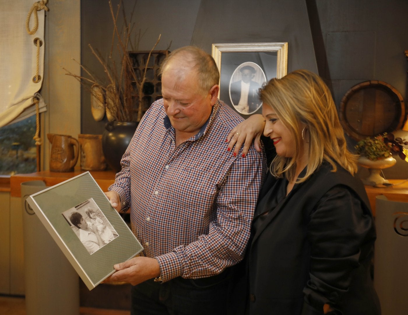 Familia.Padre e hija con una foto del fundador del llagar detrás y sosteniendo una imagen de la infancia de ella.