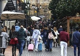 Dos jóvenes, con sus maletas, suben por una abarrotada calle Gascona.