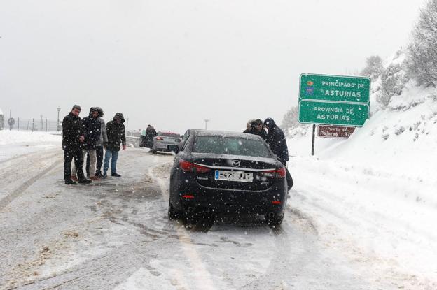 En la imagen, unos jóvenes ponen las cadenas a sus coches en Pajares. En el vídeo, las consecuencias del temporal en Asturias. 