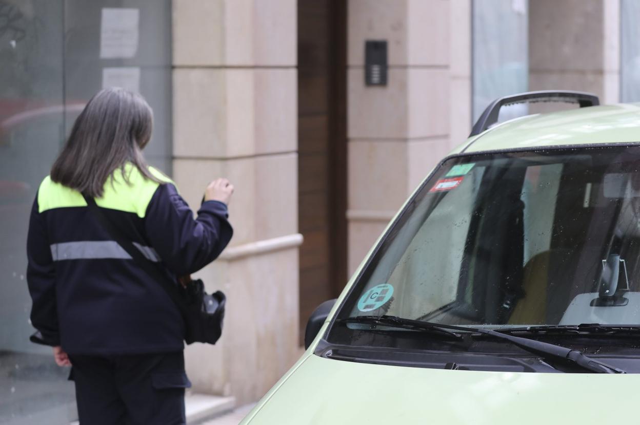 Una vigilante de la ORA comprueba el distintivo ambiental de un vehículo aparcado. 