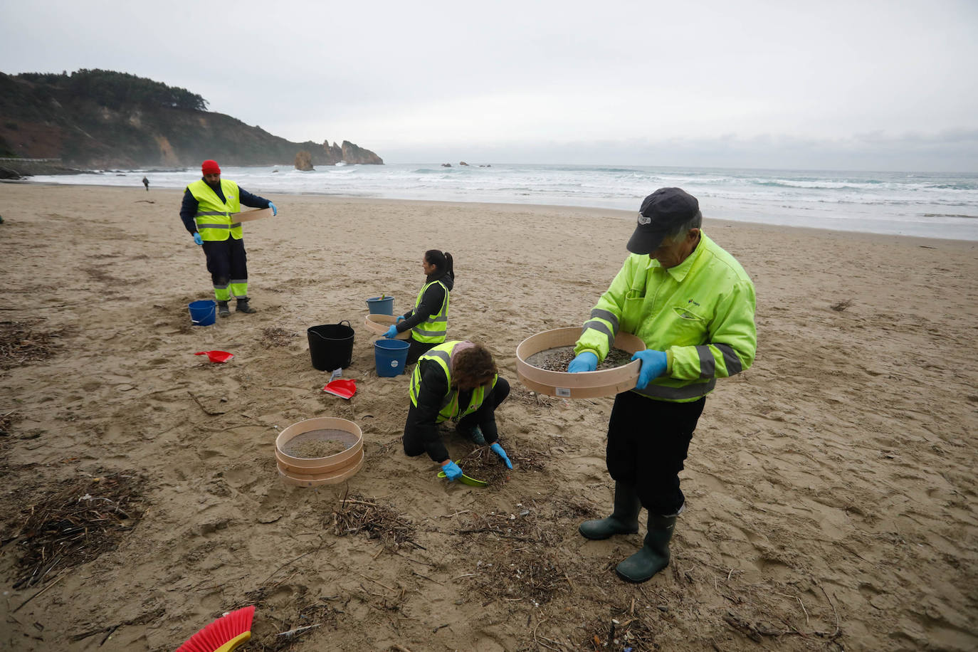 Operarios retiran los pellets o bolitas para fabricar plástico que aparecen en las playas de Asturias, tras la caída de un contenedor de un barco el pasado diciembre, esta mañana en la playa asturiana del Aguilar.