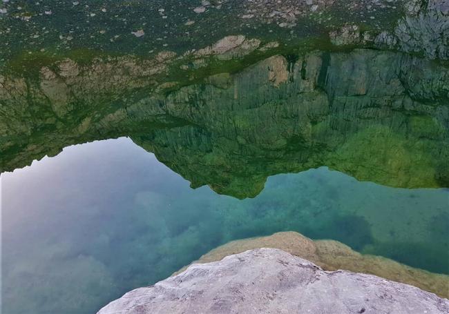 Los altos muros del Paredón del Albo reflejados en las turquesas aguas del lago de las Moñetas