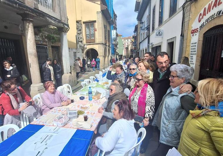 En la imagen, Adrián Barbón y Mariví Monteserín, junto a unas mujeres que disfrutan de la Comida en la Calle de Avilés en la calle Rivero. En el vídeo, el presidente del Principado habla con los medios.