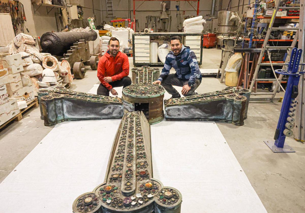 Santiago Longo y Rudy Lobosco, junto a la Cruz de la Victoria que hasta 1998 presidía la entrada a la iglesia. A la izquierda, uno de los dos cañonesde la batería baja de Cimadevilla que también estánrestaurando en su taller, Áuriga, ubicado en Avilés.