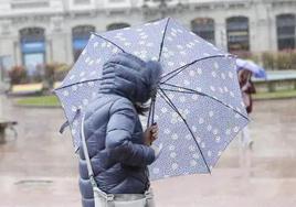 Una mujer se protege de la lluvia y el viento en una calle de Oviedo