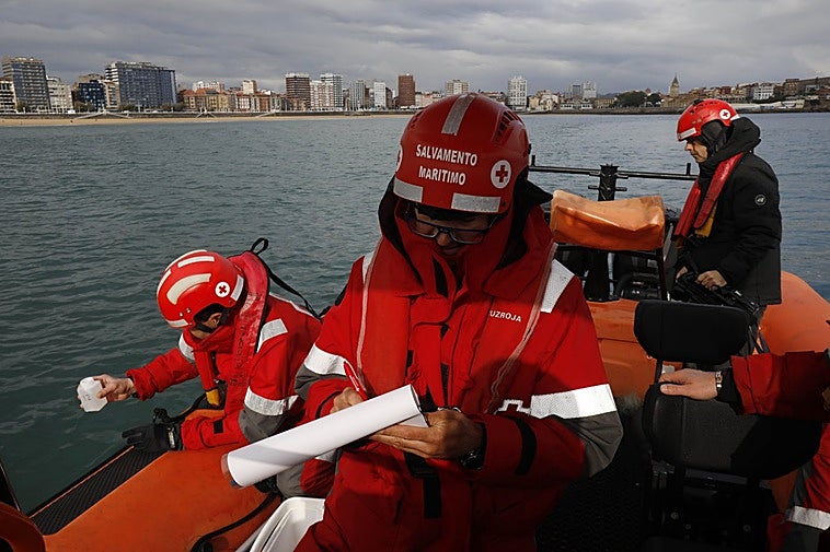 Un miembro de Cruz Roja recoge una muestra de agua frente a la playa de San Lorenzo, mientras su compañero anota los parámetros meteorológicos.