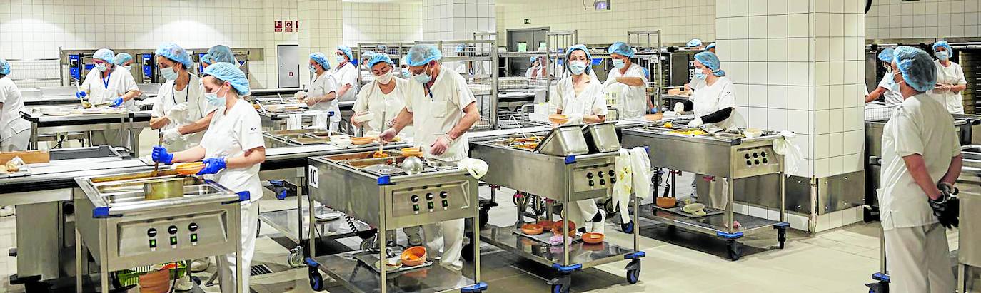 Imagen principal - La cocina. Una instalación de 1.500 metros cuadrados en la que trabajan 160 personas. En la imagen, el turno de comida sirve las bandejas en cadena, siguiendo las indicaciones dietéticas pautadas para cada paciente. Los robots. Son 14. Éste, en concreto, espera para acoplarse bajo un carro de comida, ante la mirada de Alfonso Álvarez. Taller. Todos los días se desmonta un robot para hacerle mantenimiento. Como un coche de F1. Al frente del taller está Antolín Eloy Llamas
