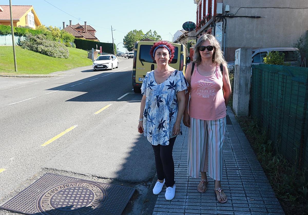 Purificación Bedriñana, presidenta de la asociación de vecinos de Roces, e Iluminada Fernández, en la parada de autobús para la que reclaman un semáforo. En el tramo se puede apreciar el flujo de tráfico.