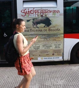 Una usuaria, ante uno de los autobuses urbanos que anuncian estos días por Gijón la Feria Taurina de Begoña