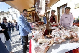 Adrián Barbón y los propietarios de una empresa de embutidos ríen por un comentario sobre uno de sus productos, las caretas de cerdo saladas, en l mercado popular celebrado en San Martín de Oscos.