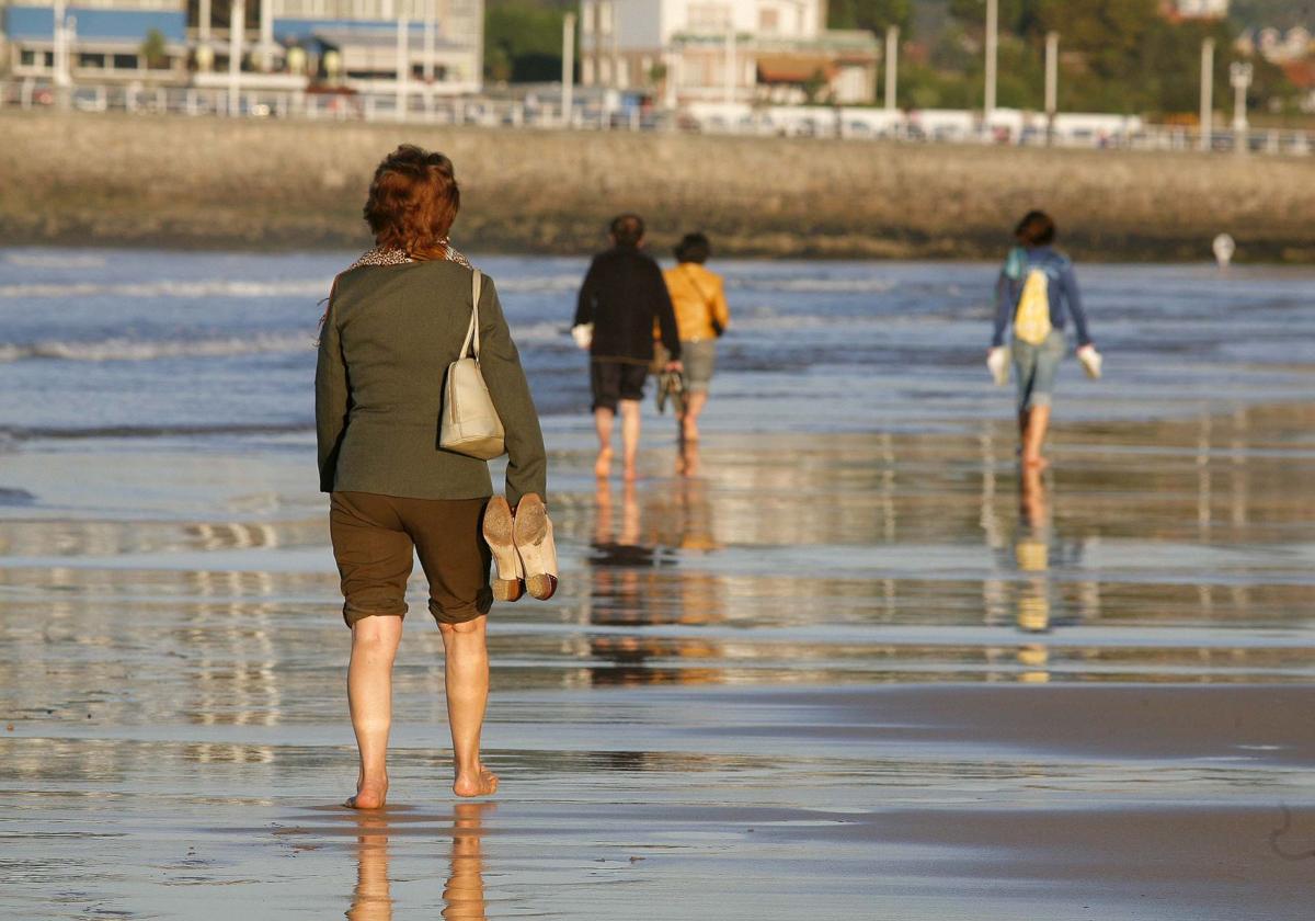 Varias personas pasean por una playa de Asturias aprovechando las suaves temperaturas.