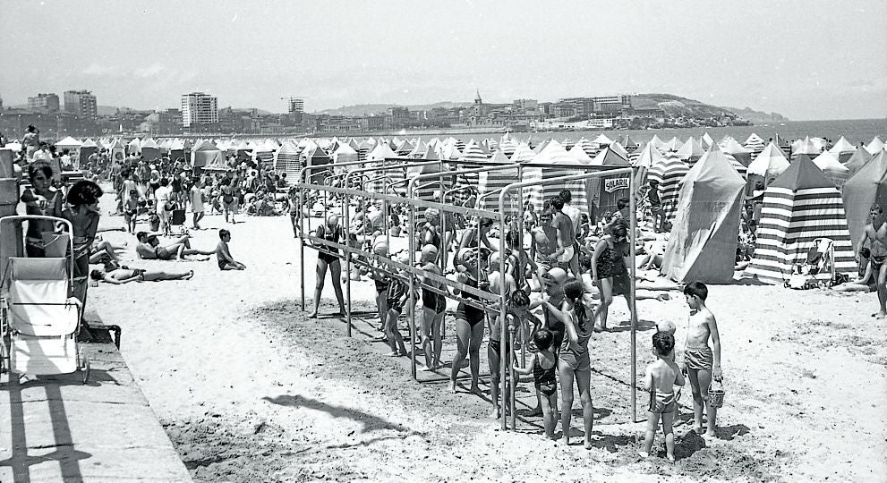 Duchas y casetas en la playa de San Lorenzo en 1965 en una instantánea captada por Manuel José Muñiz.