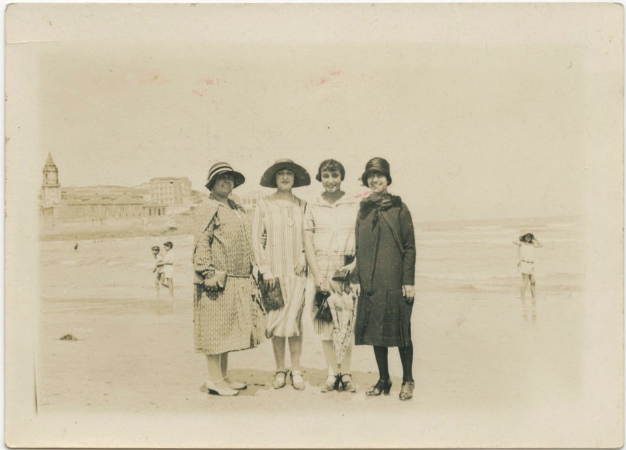 Cuatro jóvenes posan en la playa de San Lorenzo. Al fondo, la iglesia de San Pedro. El atuendo completamente oscuro de la mujer de la derecha contrasta con las tonalidades claras de los otros tres vestidos. Fotógrafo desconocido, h. 1926.