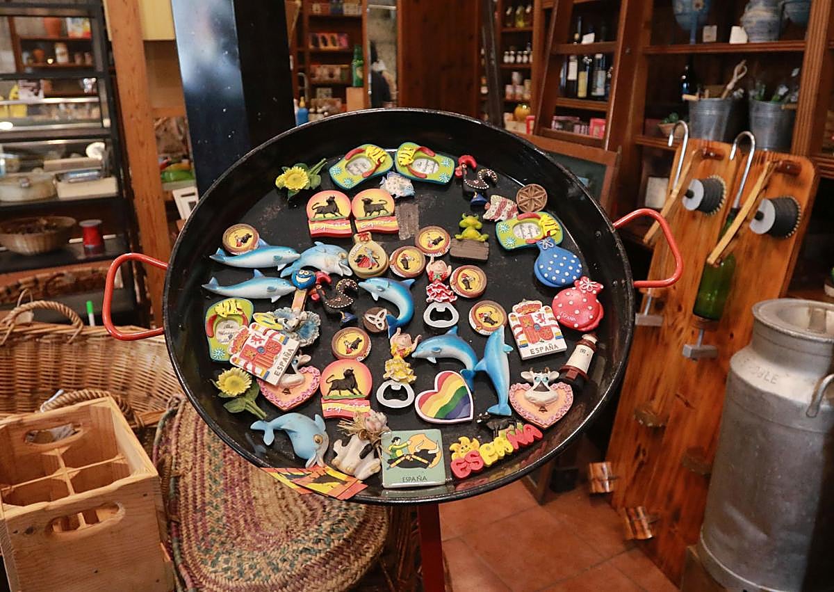 Imagen secundaria 1 - Arriba, estanterías repletas aún de objetos; a la izquierda, paellera con imanes, cestería y escanciadores y a la derecha, imanes asturianos y al fondo una lechera tradicional. 