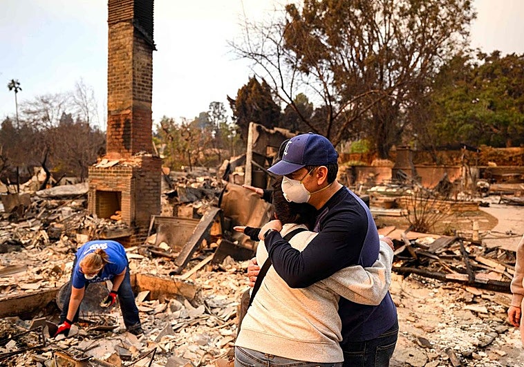 Dos personas se abrazan mientras otra busca objetos entre los escombros causados por los devastadores incendios que asolan Los Ángeles.