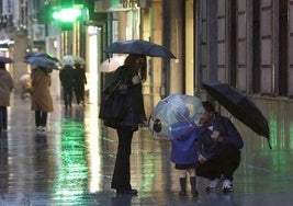 Una familia pasea, bajo la lluvia, por la calle Corrida de Gijón.