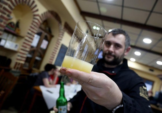 Un camarero ofrece un culín de sidra.