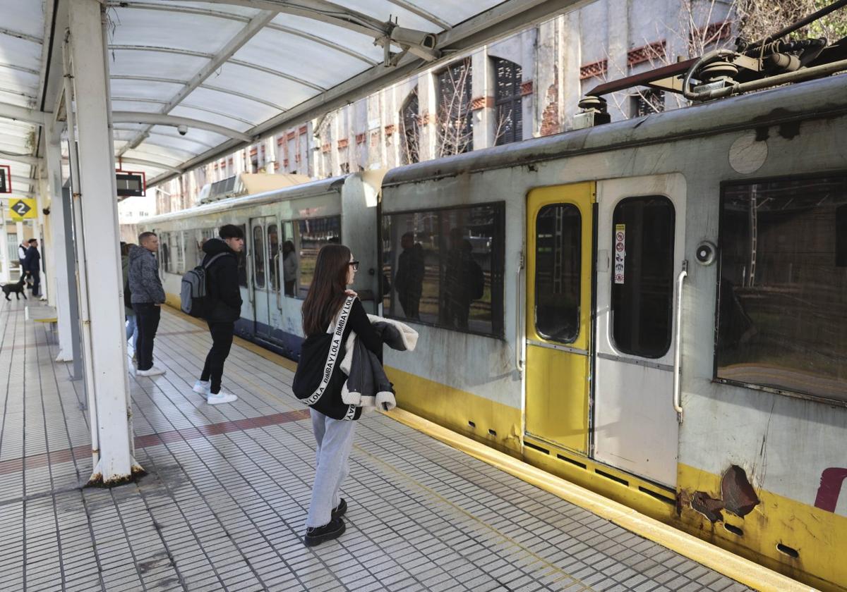 Viajeros de ancho métrico a punto de subirse a un tren sucio y con desconchones, en Avilés.