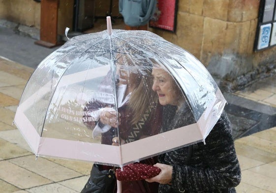 Dos mujeres se protegen de la lluvia bajo un paraguas en Oviedo.