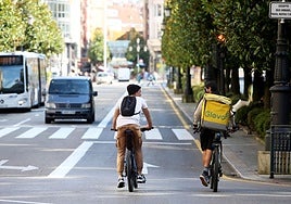 Unos jóvenes, en primer término, en bici por la calle Uría.