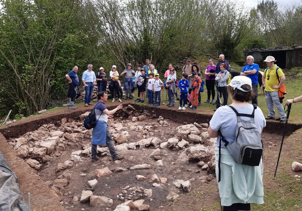 El arqueólogo Juan Ramón Muñiz explica detalles del castro de Pico Castiello a los vecinos. A sus pies, los restos descubiertos de una cabaña prerromana