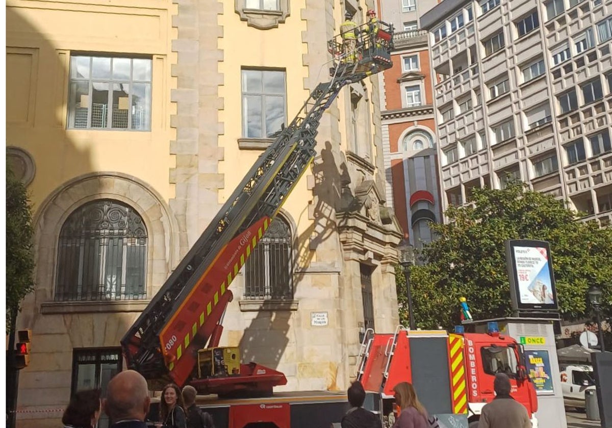 Los bomberos sanean la fachada del edificio de Correos, en Gijón
