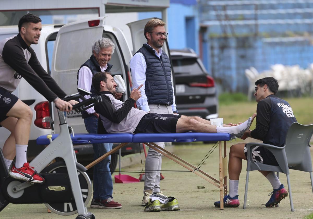 El fisio Abel Canteli trata a Jose Martínez sobre la camilla, con Kevin Bautista a la derecha ejercitándose en una bicicleta estática.